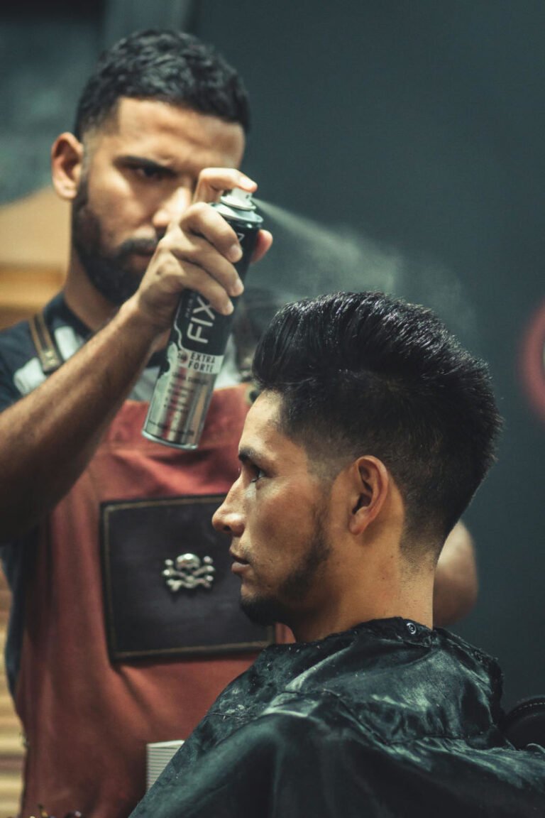 Barbeiro aplicando spray fixador no cabelo de um cliente para finalizar um corte moderno com topete alto (pompadour).